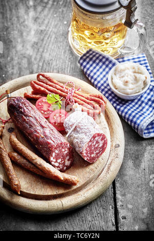 Auswahl von getrockneten würzigen wild Wildbret Würstchen mit einem Dip und Becher ale auf einem rustikalen Holzbrett und Tisch serviert Stockfoto