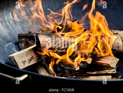 Frisch lit Grill Feuer mit Logs des brennenden Holzes über kleine Späne der Späne in einen tragbaren Grill Stockfoto