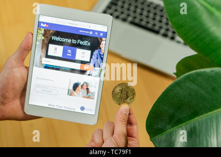 Ljubljana, Slowenien 29.4.2019: Unternehmer halten Computer Tablet mit geöffneten Fedex website und Bitcoin Münze auf einem Schreibtisch Stockfoto