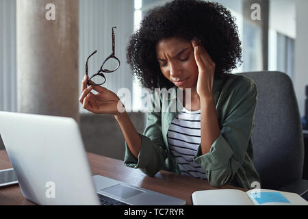 Überarbeitet African Business Frau mit Kopfschmerzen im Büro Stockfoto