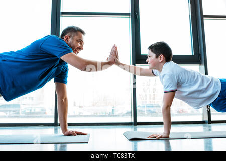 Vater und Sohn gegen die Hohe fünf Zeichen, während Push up tun Übung im Fitnessstudio Stockfoto
