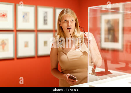 Positive Frau mit Brille und Smartphone Besuch von historischen Museum und Vitrinen mit Exponaten auf der Suche Stockfoto