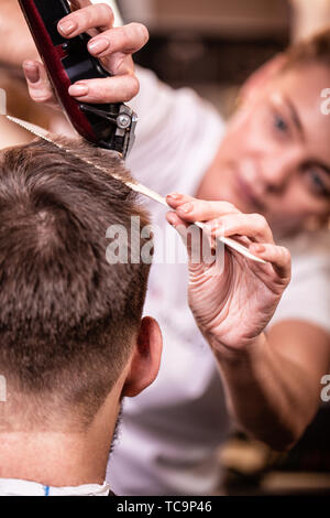 Der Master schneidet die Haare und Bart eines Mannes in einem Friseursalon, Ein Friseur ist ein Haarschnitt für einen jungen Mann. Schönheit Konzept, Self Care. Stockfoto