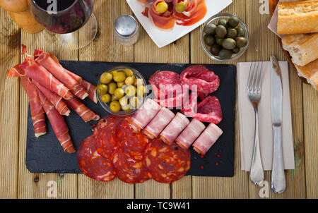 Blick von oben auf die in Scheiben geschnittenen Spanisch trocken-cured Gammon, Chorizo, Salami und Speck serviert mit grünen Oliven auf schiefer Board Stockfoto