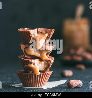 Stapel von vegane Schokolade Tassen mit Karamell auf dunklen Tischplatte. Hausgemachte vegetarische Chocolate Caramel Cups mit rohem Kakao Schokolade. Ideen und Rezepte für gesunde Süßigkeiten und Desserts. Kopieren Sie Platz für Text Stockfoto