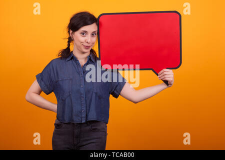 Lächelnd schöne Frau mit einem leeren dachte, Blase, und wenn man die Kamera im Studio auf gelben Hintergrund. Lustige junge Frau mit leeren Plakat. Stockfoto