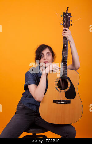 Portrait von schönen jungen Sänger ihre acustic Gitarre im Studio auf gelben Hintergrund. Ziemlich kaukasische Frau mit Musikinstrument. Stockfoto