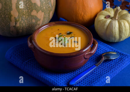 Kürbis Suppe in ein irdenes Gefäß mit Petersilie, Olivenöl und Kürbiskerne mit Löffel. Vegan und gesundes Essen. Dunkelblauen Hintergrund. Stockfoto