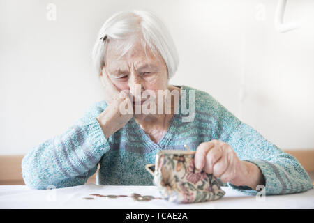 Betroffene ältere Frau am Tisch sitzen zählen Geld in Ihrem Portemonnaie. Stockfoto