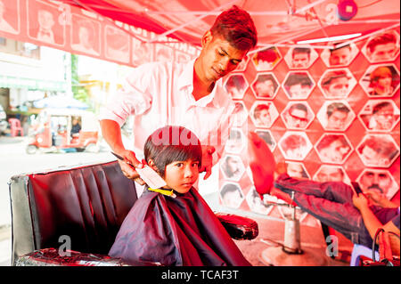 Ein schüchterner kleiner kambodianischer Junge bekommt seine Haare in einem typischen Barbershop im Freien in Phnom Penh, Kambodscha geschnitten. Stockfoto