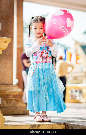 Ein hübsches kleines Kambodschanisches Mädchen wirft in ihrem gefrorenen Kleid mit einem Ballon außerhalb der Königspalast in Phnom Penh, Kambodscha. Stockfoto