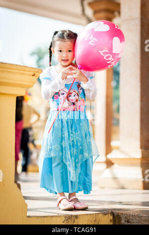 Ein hübsches kleines Kambodschanisches Mädchen wirft in ihrem gefrorenen Kleid mit einem Ballon außerhalb der Königspalast in Phnom Penh, Kambodscha. Stockfoto