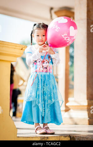 Ein hübsches kleines Kambodschanisches Mädchen wirft in ihrem gefrorenen Kleid mit einem Ballon außerhalb der Königspalast in Phnom Penh, Kambodscha. Stockfoto