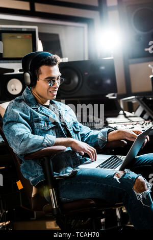 Lächelnd Mixed Race Sound Hersteller in Kopfhörer mit Laptop im Recording Studio Stockfoto
