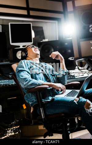 Lächelnd Mixed Race Sound Hersteller in Kopfhörer Musik hören Weiß im Büro Stuhl Stockfoto