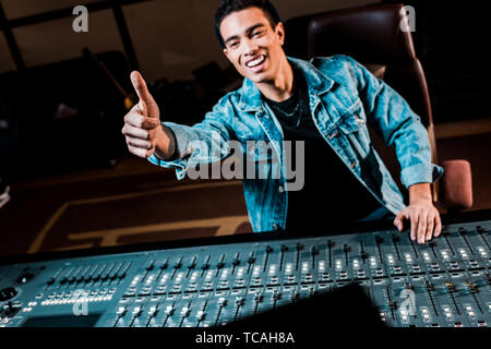 Lächelnd Mixed Race Sound Hersteller zeigen Daumen hoch, während er in der Nähe von Mischpult in Recording Studio Stockfoto