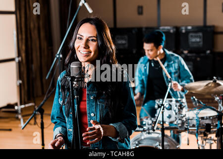 Hübsche Frau zu singen, während gemischte Rasse Musiker Schlagzeug spielen im Recording Studio Stockfoto