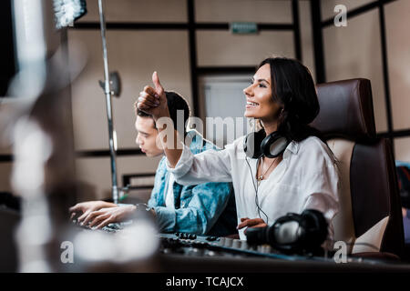 Selektiver Fokus der hübscher Ton Produzent der Ohrhörer am Mischpult in der Nähe von gemischten Rennen Freund arbeiten Stockfoto