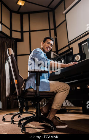 Lächelnd Mixed Race Sound Hersteller in Bürostuhl in Recording Studio und Kamera sitzen Stockfoto