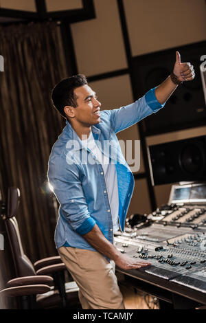 Lächelnd Mixed Race Sound Hersteller zeigen Daumen hoch, während am Mischpult arbeiten Stockfoto