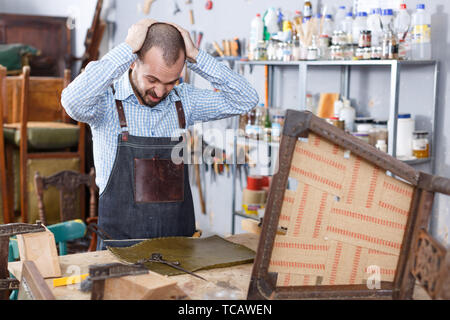 Verärgert Arbeiter mit Qualität des Leders für Polsterung Stuhl in Reparatur Möbel Workshop unzufrieden Stockfoto