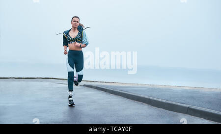 Sie sind stärker als Sie denken. Erstaunlich stark behinderte Frau in Sportkleidung läuft im Freien in der Nähe des Meeres. Motivation. Sport Konzept. Behinderte Sportler Stockfoto
