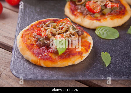 Mini Pizza belegt mit Schinken, grüne Oliven, Tomaten und frischem Basilikum. Hausgemachte Speisen. Konzept für einen leckeren und herzhaftes Essen. Schwarzen Hintergrund. Stockfoto