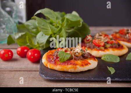 Mini Pizza belegt mit Schinken, grüne Oliven, Tomaten und frischem Basilikum. Hausgemachte Speisen. Konzept für einen leckeren und herzhaftes Essen. Holz- Hintergrund. Stockfoto