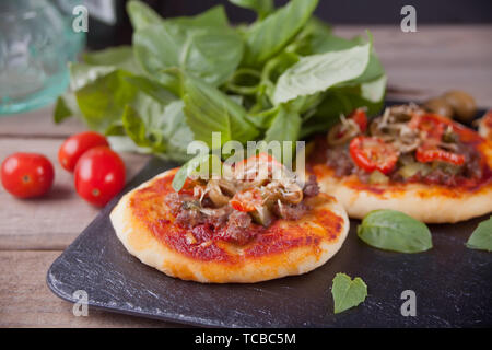 Mini Pizza belegt mit Schinken, grüne Oliven, Tomaten und frischem Basilikum. Hausgemachte Speisen. Konzept für einen leckeren und herzhaftes Essen. Holz- Hintergrund. Stockfoto