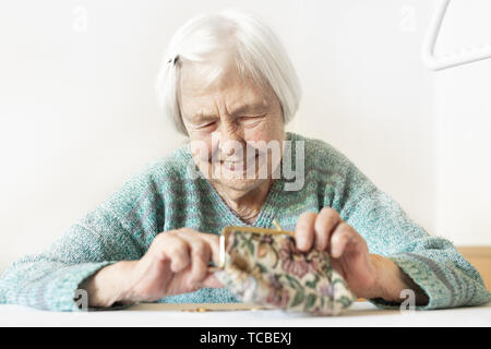 Freundliche ältere 96 Jahre alte Frau am Tisch sitzen zu Hause glücklich mit Ihr Vorsorgeguthaben in Ihrem Portemonnaie nach Rechnungen bezahlen. Stockfoto