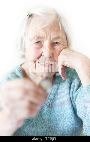 Fröhliche ältere 96 Jahre alte Frau, die zu Hause am Tisch sitzt, glücklich mit einer Münze in der Hand. Sparen für den Ruhestand und finanzielle Planung Konzept Stockfoto