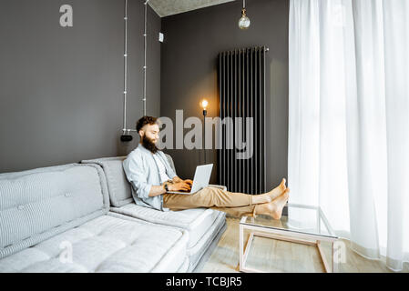 Kreative bärtiger Mann arbeiten mit Laptop, sitzen auf der Couch im Wohnzimmer zu Hause. Stockfoto