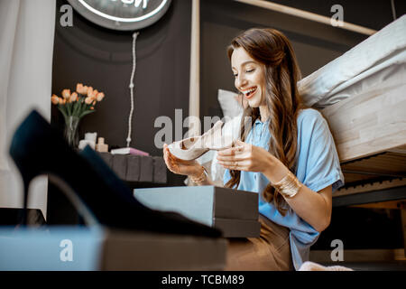 Junge Frau auspacken Pakete mit Schuhen, Gefühl zufrieden mit neuen on-line-Erwerbe, im Schlafzimmer zu Hause sitzen Stockfoto