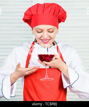 Somellier mit Weinglas. Frau in Cook hat und Schürze. professioneller Koch in der Küche. Küche. Hausfrau Rotwein trinken. glückliche Frau. Grüße an Freunde. Sommelier Prüfung Wein. Das ist perfekter Wein. Stockfoto