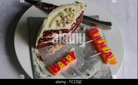 Bunte HAPPY BIRTHDAY Gruß Kerzen. Scheibe der Red Velvet Cake auf einer weißen Platte Stockfoto