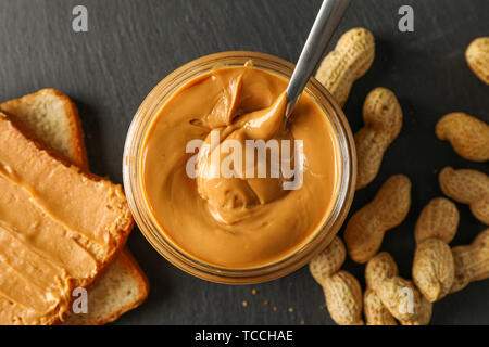 Glas Glas mit Erdnussbutter und Löffel, Erdnuß, Peanut butter Sandwich und Schneidbrett auf hölzernen Hintergrund, Platz für Text und Nahaufnahme Stockfoto