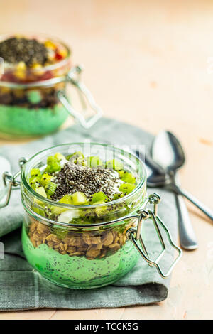 Zwei Chia Samen Pudding mit Matcha Grüntee, Kiwi und Müsli, orange in Gläsern auf Hellrosa konkreten Hintergrund. Gesundes Frühstück. Stockfoto