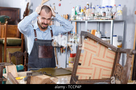 Verärgert Arbeiter mit Qualität des Leders für Polsterung Stuhl in Reparatur Möbel Workshop unzufrieden Stockfoto