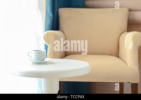 Weißer Tee Tasse und Untertasse auf einem runden weißen Tisch gegen eine beige Stuhl Stockfoto