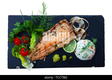 Bild von köstlich gebratenes Forellenfilet mit Reis und Grünen auf schwarzem Teller. Auf weissem Hintergrund Stockfoto