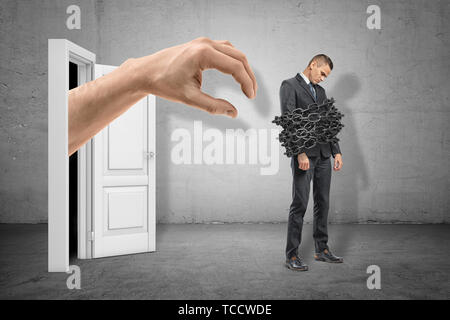 Volle Länge Seitenansicht des traurigen kleinen Geschäftsmann stehend mit Ketten um seinen Körper und die große Hand, die sich aus der Tür hinter ihm. Stockfoto