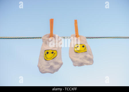 Weiße Socken mit einem gelben Smiley Emoticon hängen an einem Seil mit Wäscheklammern. Blauer Himmel Stockfoto