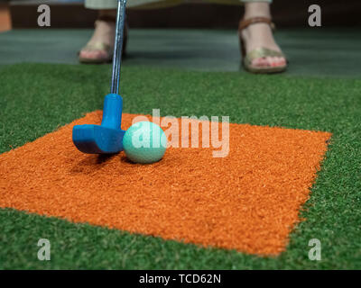 Blau Putter auf Rasen aufgereiht neben Green Golf Ball auf Minigolfkurs mit Frau spielen Stockfoto