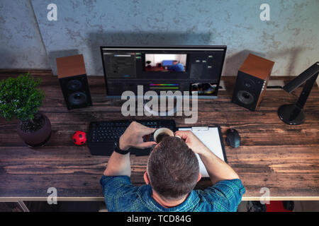 Geschäftsmann Anhalten von Kaffee während der Arbeit an seinem Schreibtisch im Büro vor einem großen PC-Bildschirm mit Foto und Bearbeiten von Windows Stockfoto