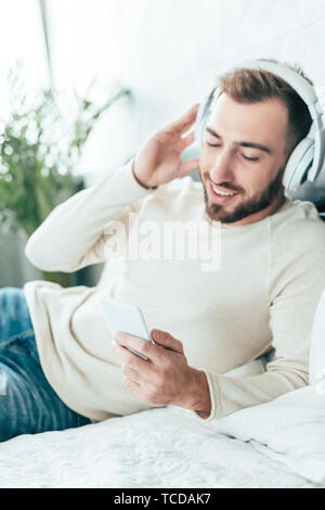 Fröhliche bärtiger Mann mit Smartphone beim Hören von Musik über Kopfhörer Stockfoto