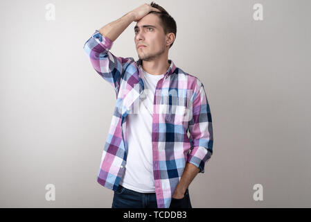 Porträt eines jungen Mannes in einem Plaid Shirt umgekippt, seinen Kopf, auf grauem Hintergrund Stockfoto
