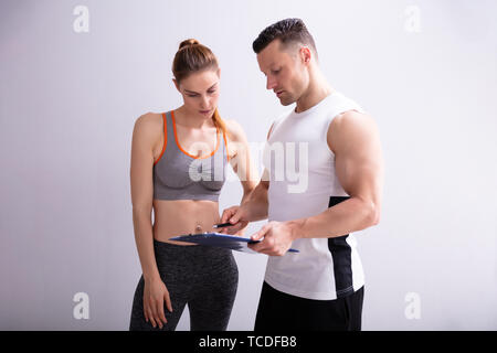 Junge Trainer und sportliche Frau diskutieren Ihre Fortschritte an der Turnhalle Stockfoto