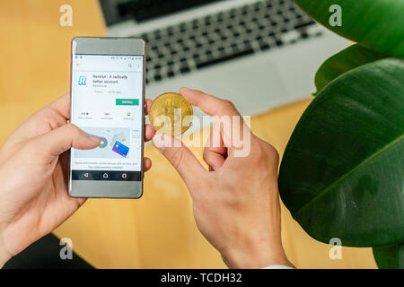 Ljubljana, Slowenien 29.4.2019: Unternehmer holding Smartphone und versuchen revolut App und Bitcoin Münze auf einem Schreibtisch zum Download Stockfoto