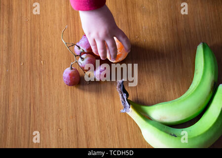 Baby s Hand manipulieren von verschiedenen Früchten auf einem Holztisch Stockfoto