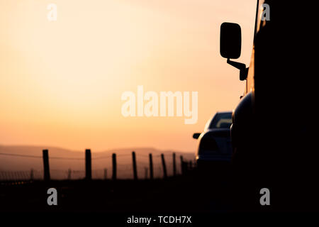 Zwei geparkte Autos in Silhouette sitzen gegen einen pastellfarbenen Sonnenuntergang im Peak District National Park in Großbritannien Stockfoto